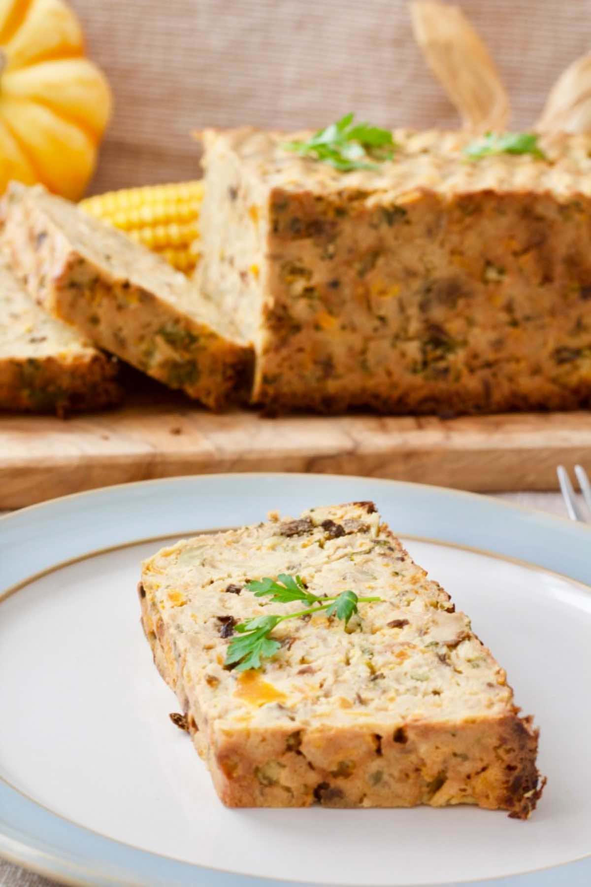 Veggie loaf slice on a plate garnished with fresh parsley, loaf in the background.