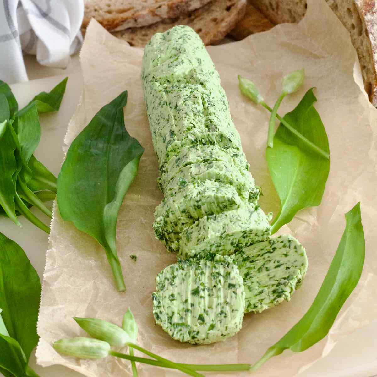 Wild garlic butter log with garlic leaves and flowers scattered around it.