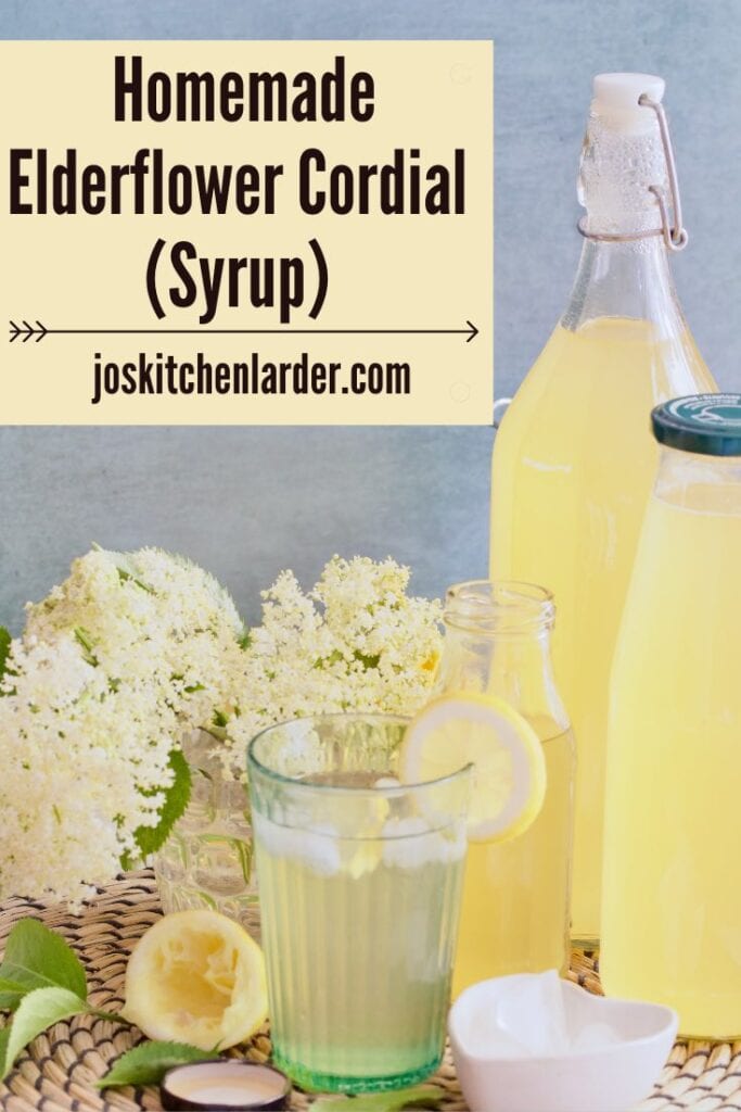 Small glass with diluted elderflower syrup with flowers behind and bottles of cordial.