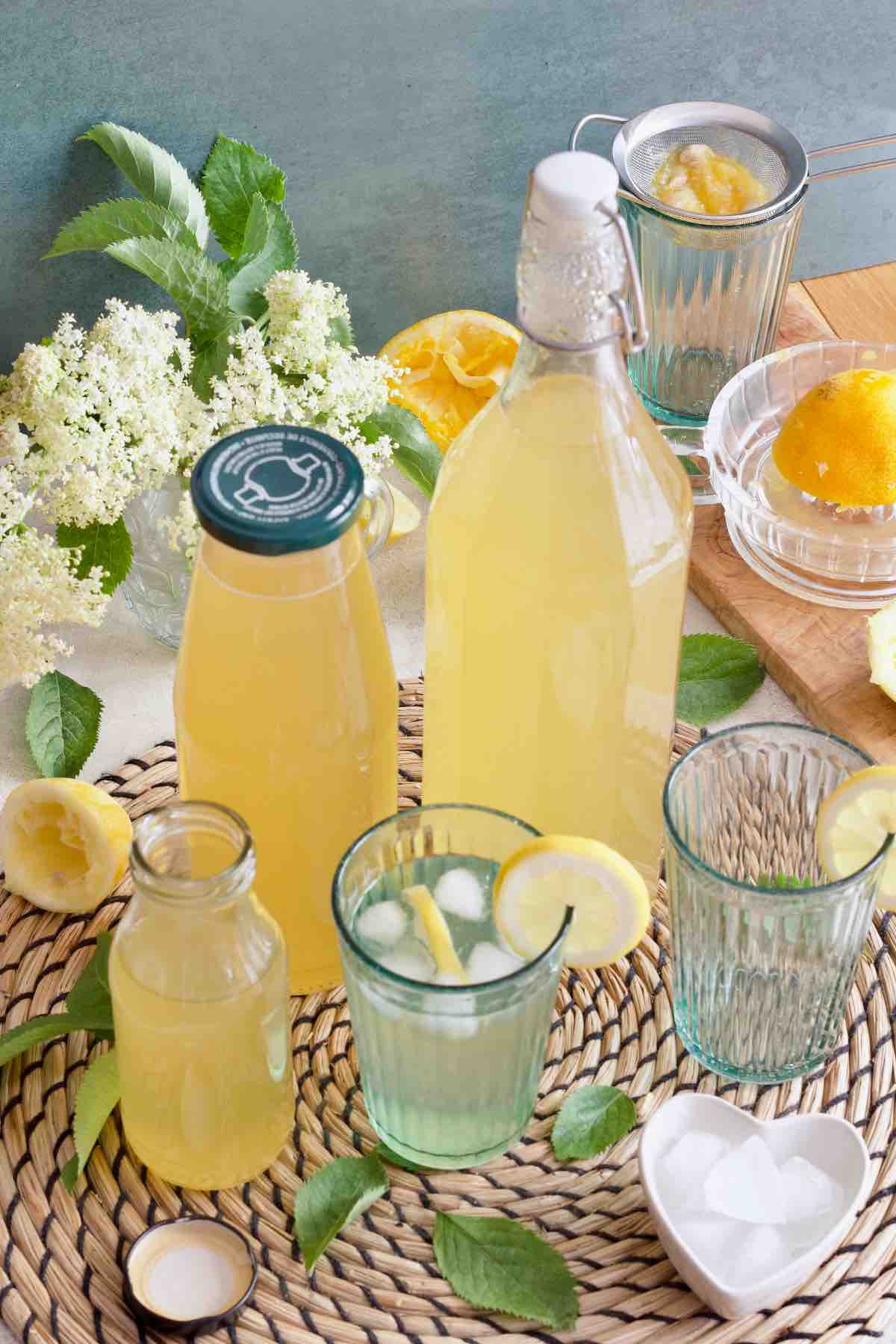 Bottles filled with elderflower cordial, glasses, ice, elderflowers.