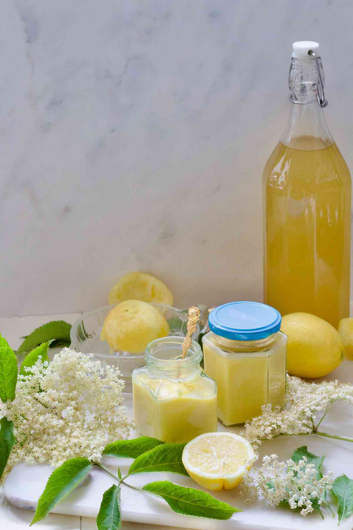 Spread consisting of elderflower cordial, two jars with curd, lemons and elderflowers.