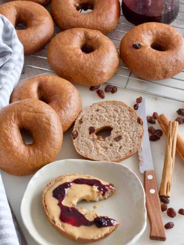 Bagel with peanut butter and jam on a small plate with more bagels around.