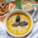 Butternut squash and red lentil soup in a bowl garnished with parmesan and three pan fried sage leaves.