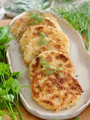 Platter with a row of kohlrabi schnitzel slices garnished with dill.