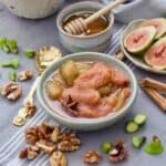 Fig compote in a bowl with fig ends, walnuts, cinnamon sticks scattered around.