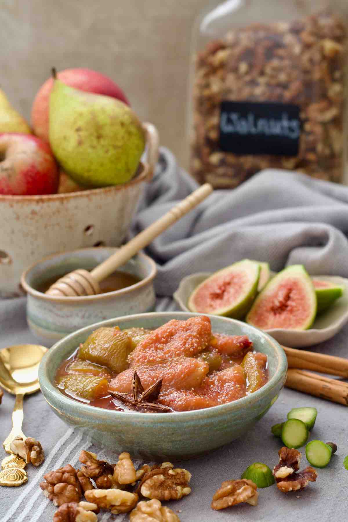 Fig compote in a bowl, fig halves, honey, fruits and nuts around it.
