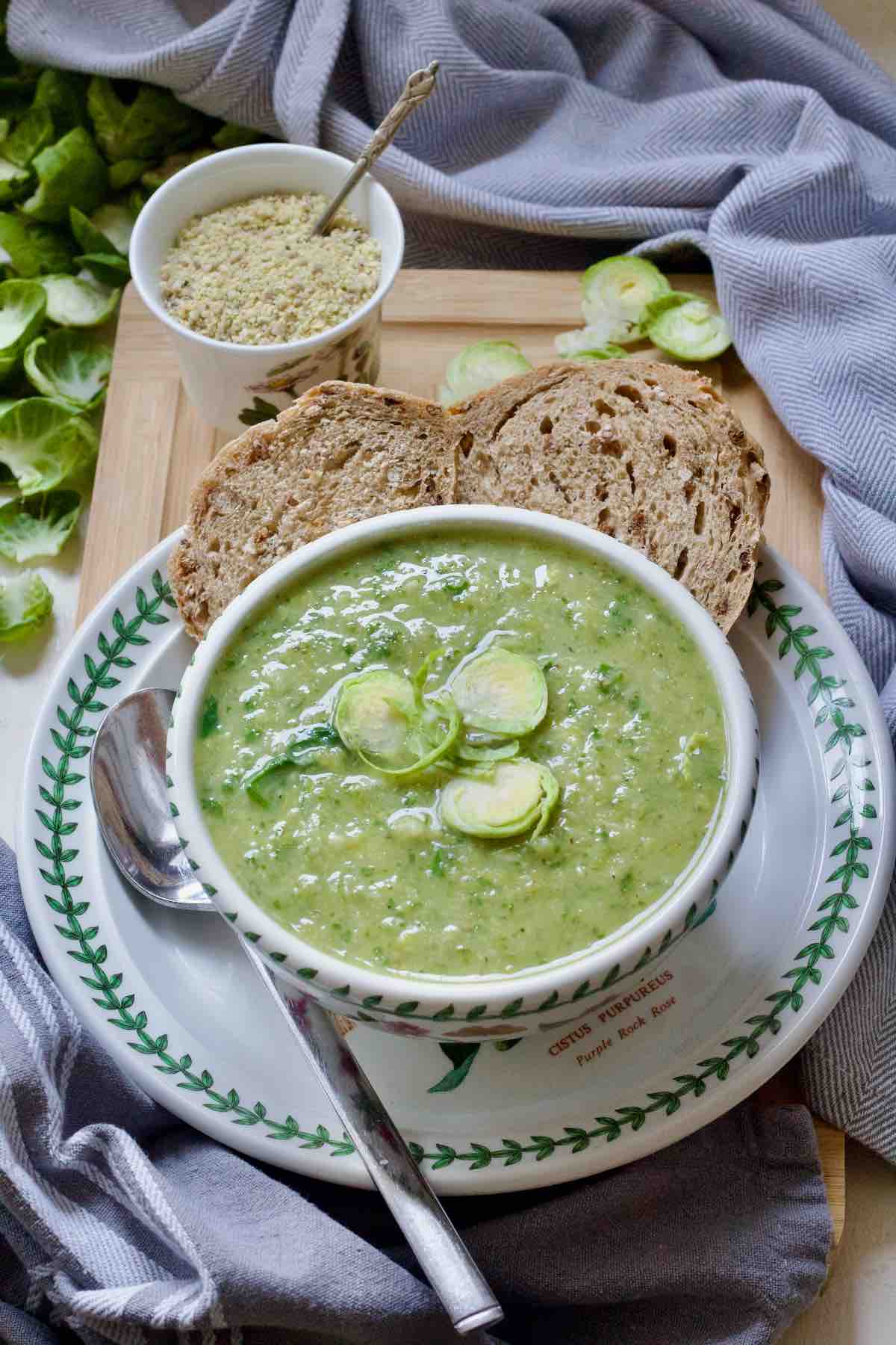 Bowl of Brussels sprouts soup garnished with shredded sprouts on a plate with granary bread slices.