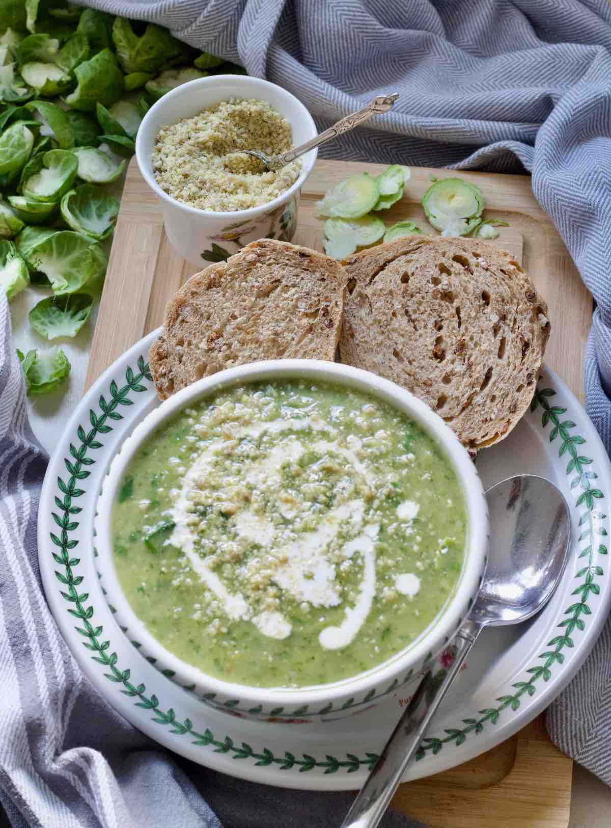 Bowl of Brussels sprouts soup on a plate with a spoon and granary bread slices.