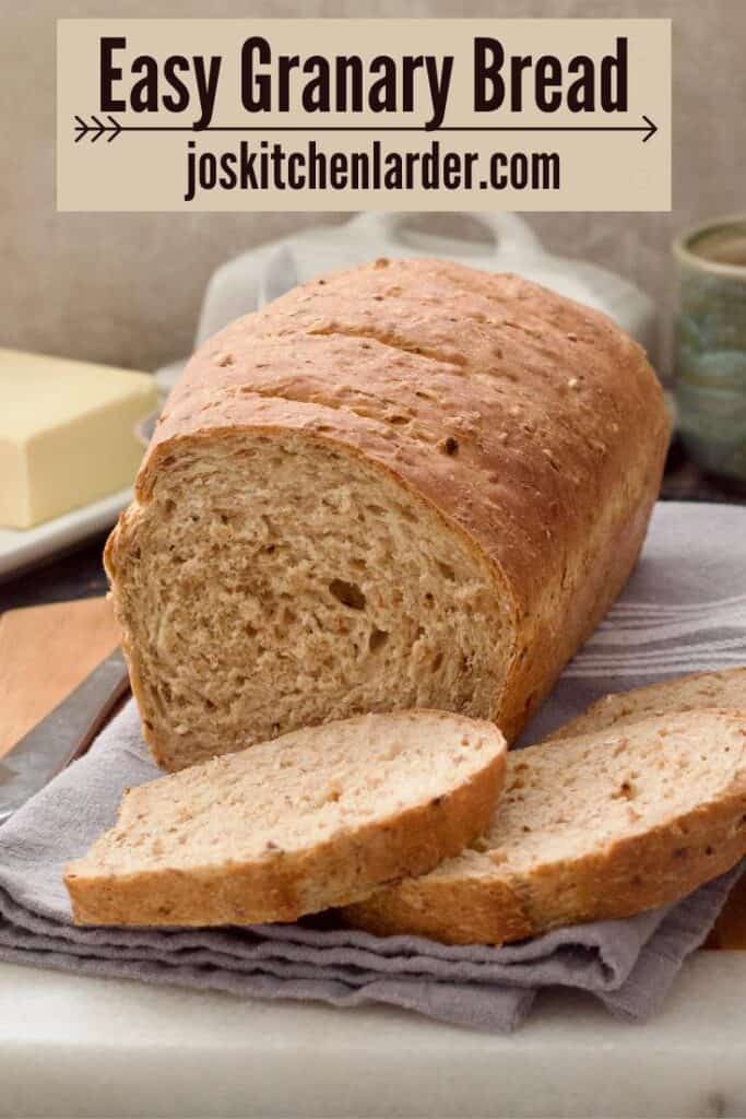 Close up of granary bread loaf with two slices cut in front of it.