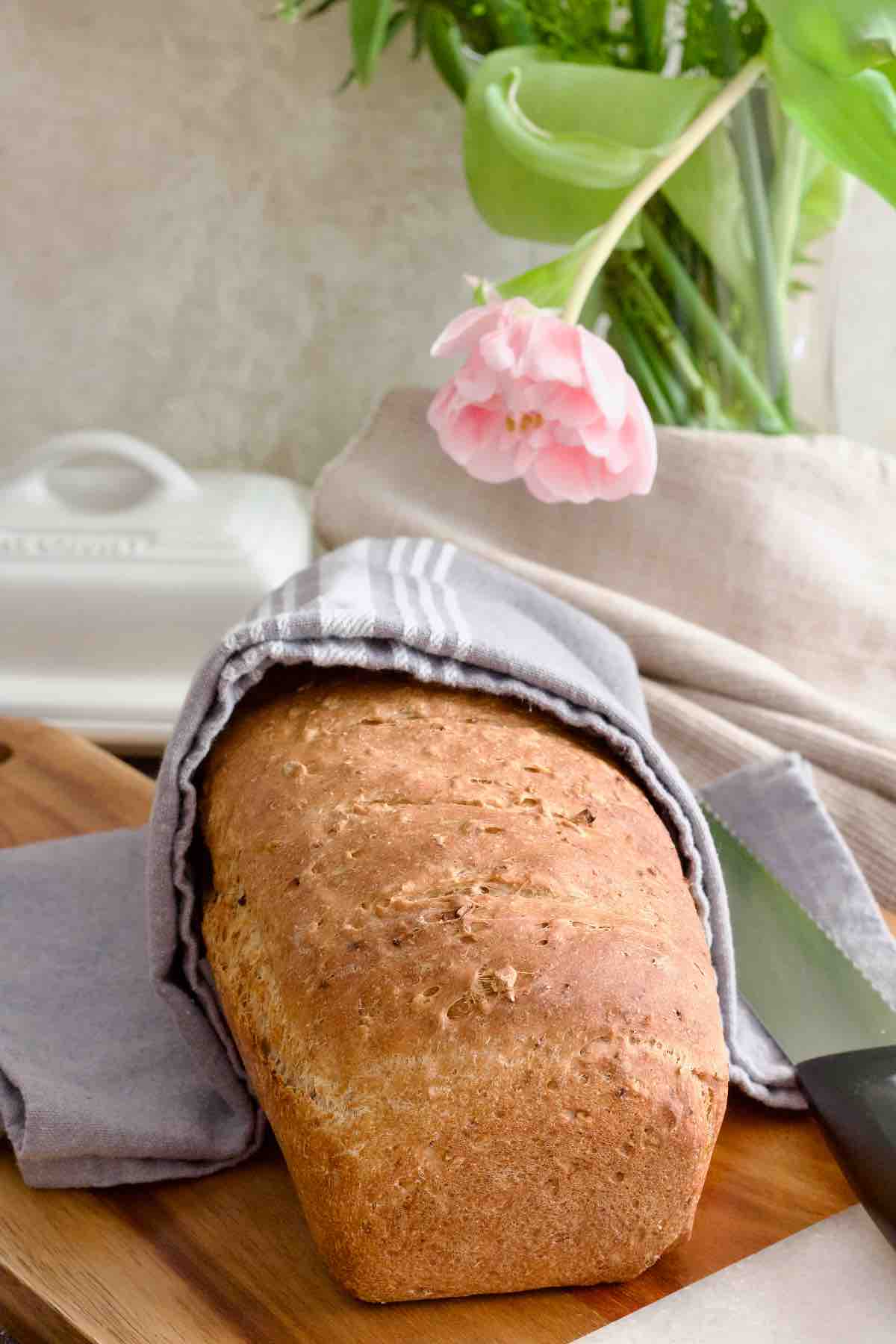 Freshly baked granary bread semi covered with kitchen towel.