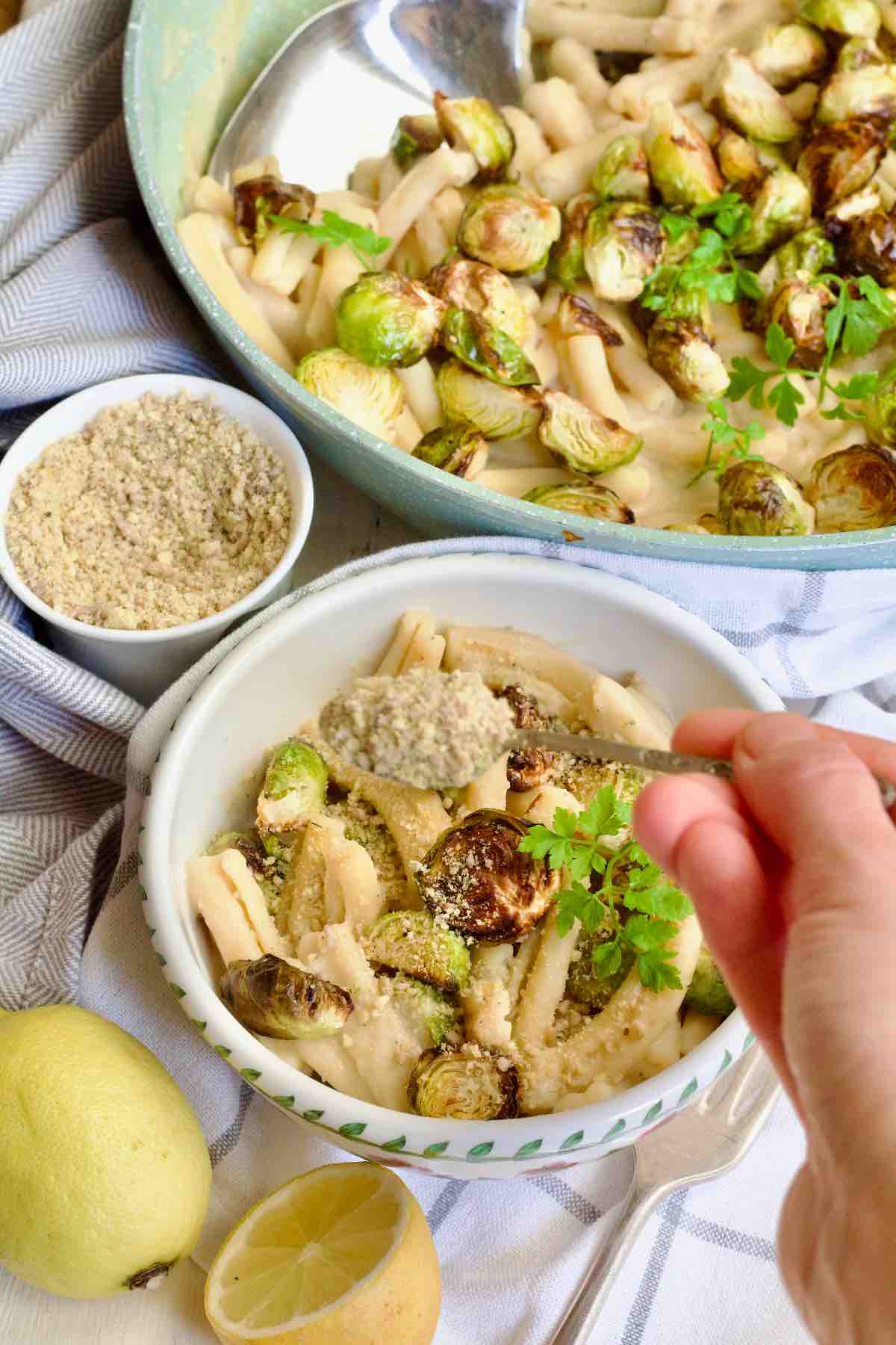 Hand sprinkling some vegan parmesan over creamy pasta in a bowl.