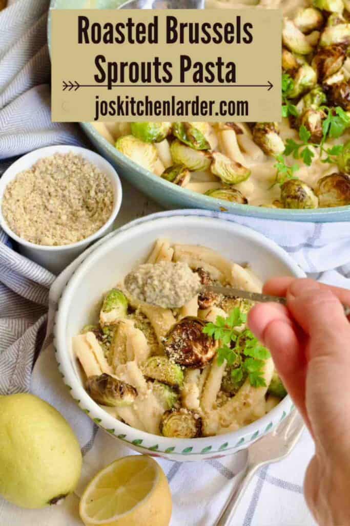 Hand sprinkling some vegan parmesan over creamy pasta in a bowl.
