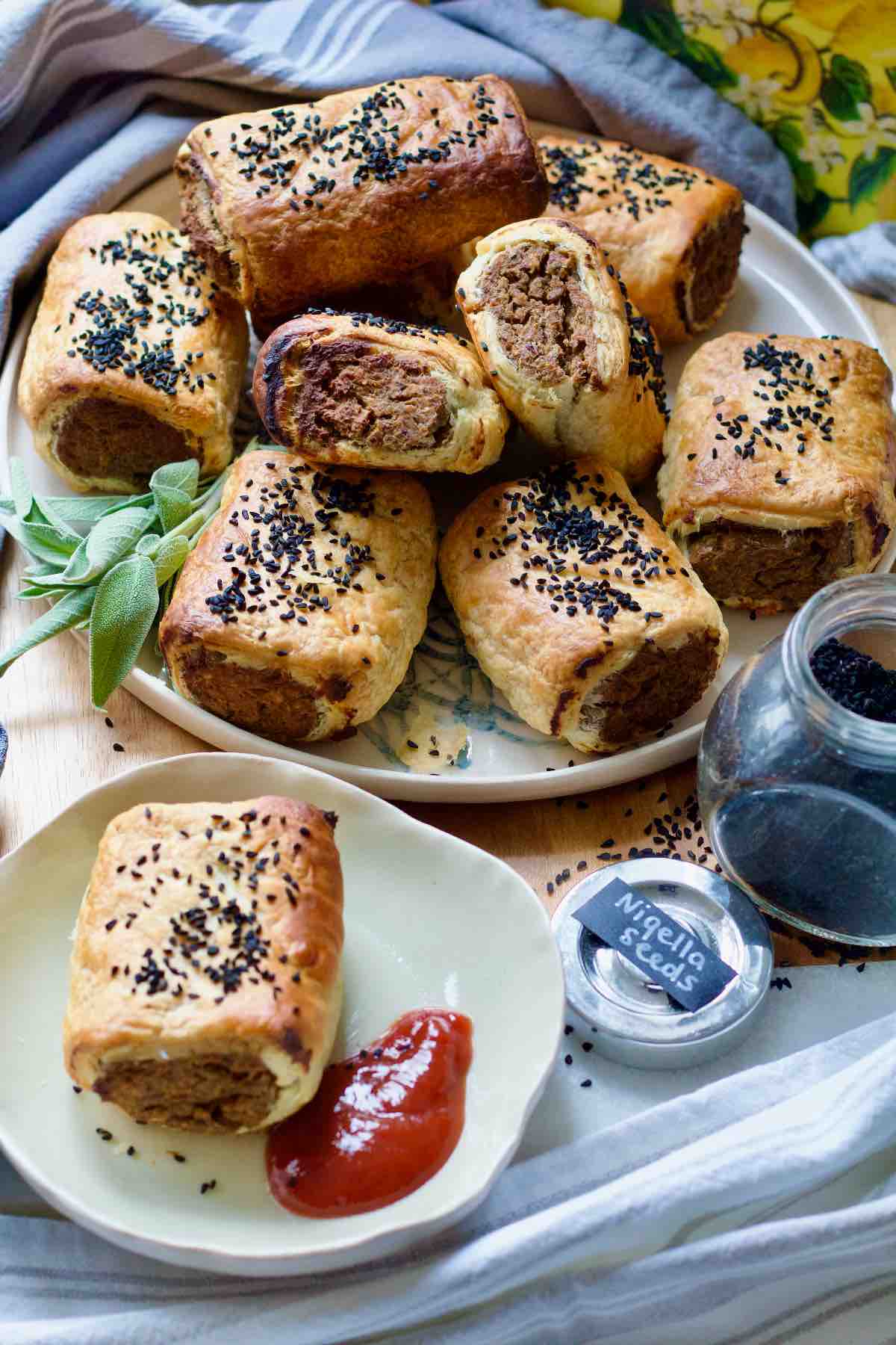 Sausage rolls piled up on a plate and one on a separate plate served with ketchup.