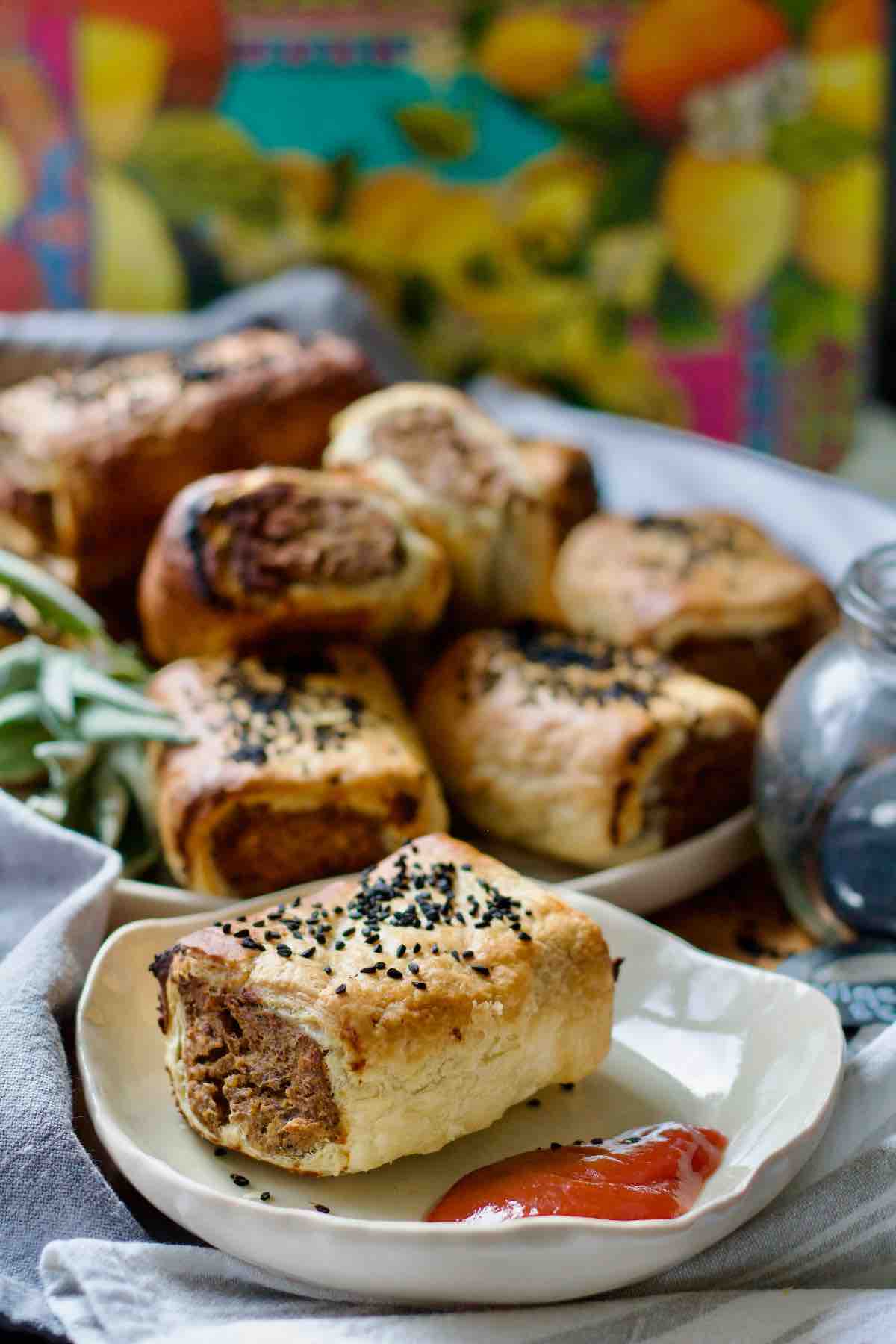 Tofu and mushroom sausage roll on a plate and more on a plate in the background.