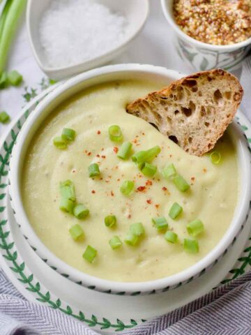 Cauliflower, leek and potato soup in a bowl with a piece of sourdough.