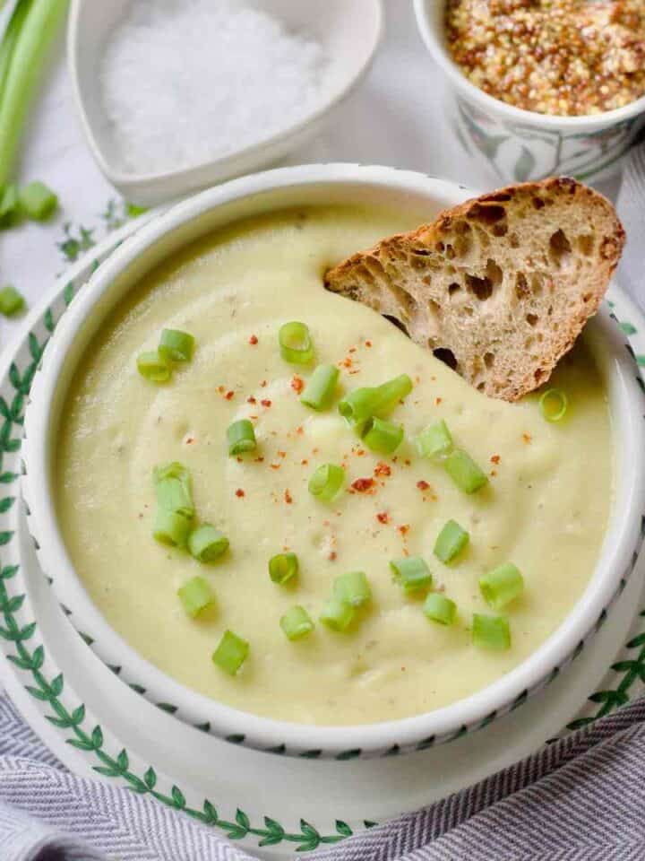 Cauliflower, leek and potato soup in a bowl with a piece of sourdough.