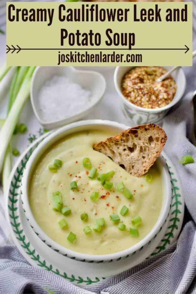Served portion of cauliflower leek and potato soup in a bowl with garnish and piece of bread in a soup.