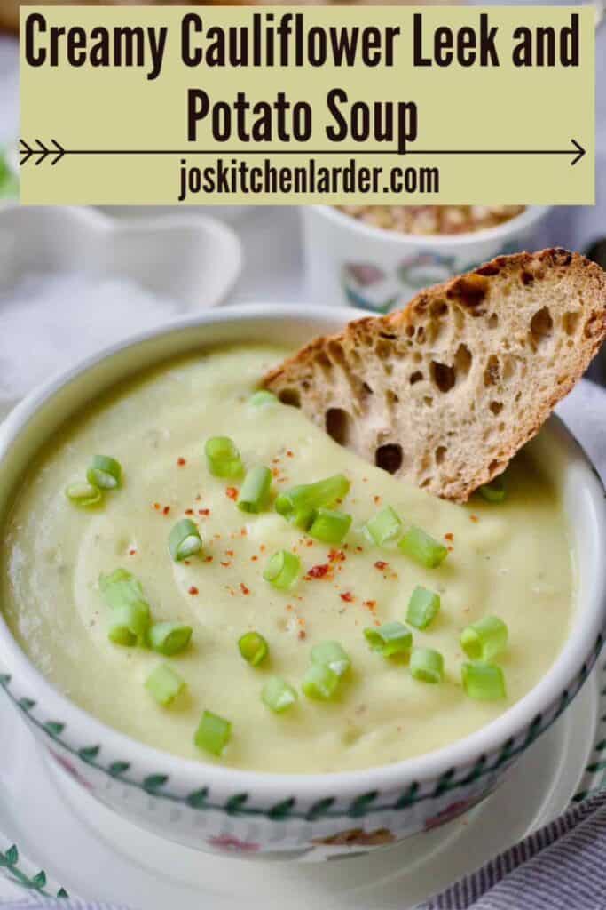 Close up of cauliflower, leek and potato soup garnished with spring onions and chilli flakes with slice of bread.