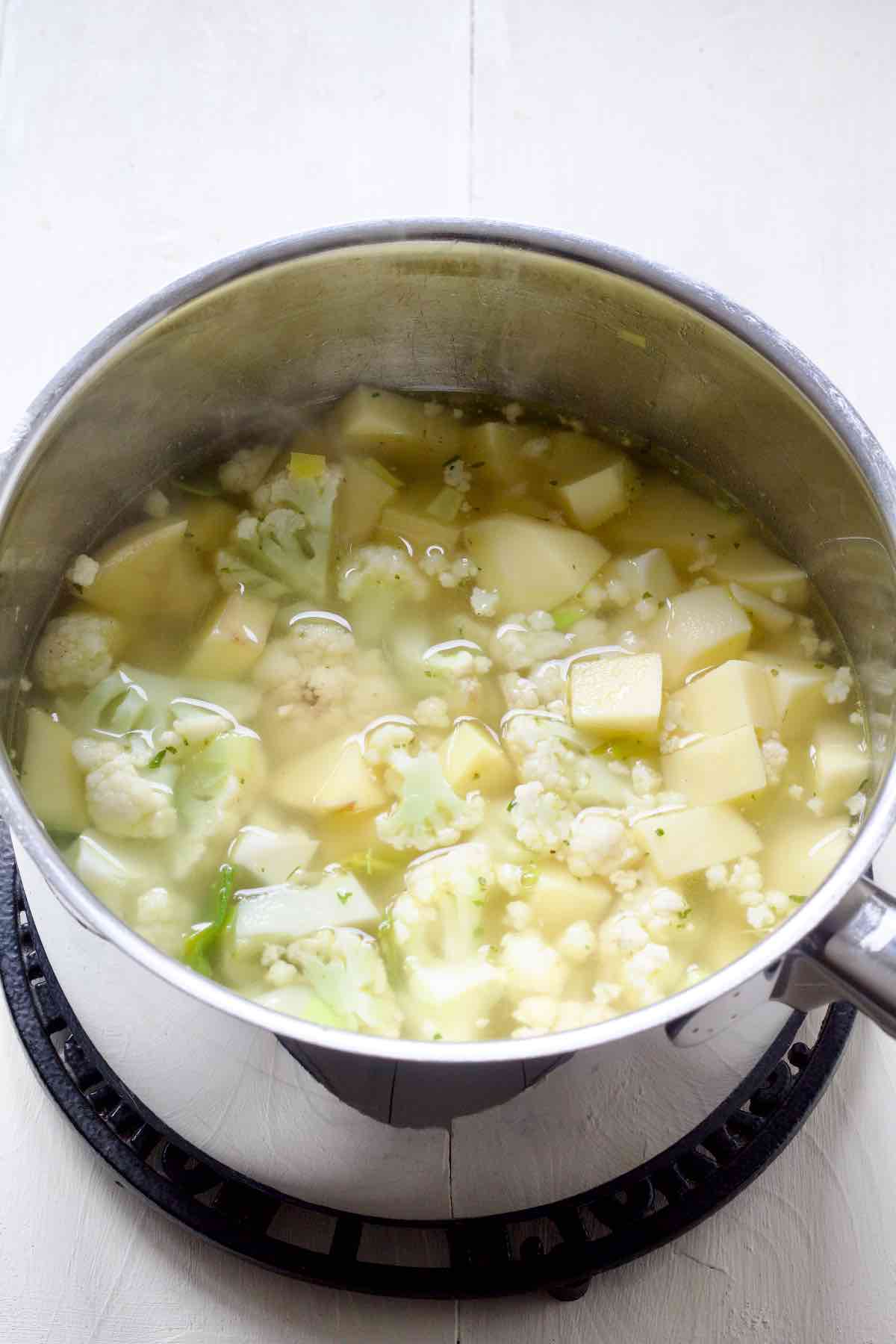 Cauliflower, potatoes and stock in a saucepan with leeks, garlic and herbs.