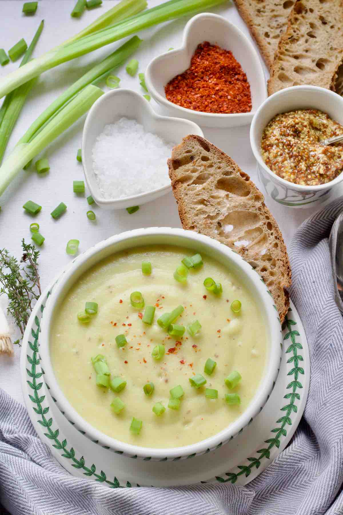 Served portion of garnished cauliflower leek and potato soup in a bowl with bread on a plate.