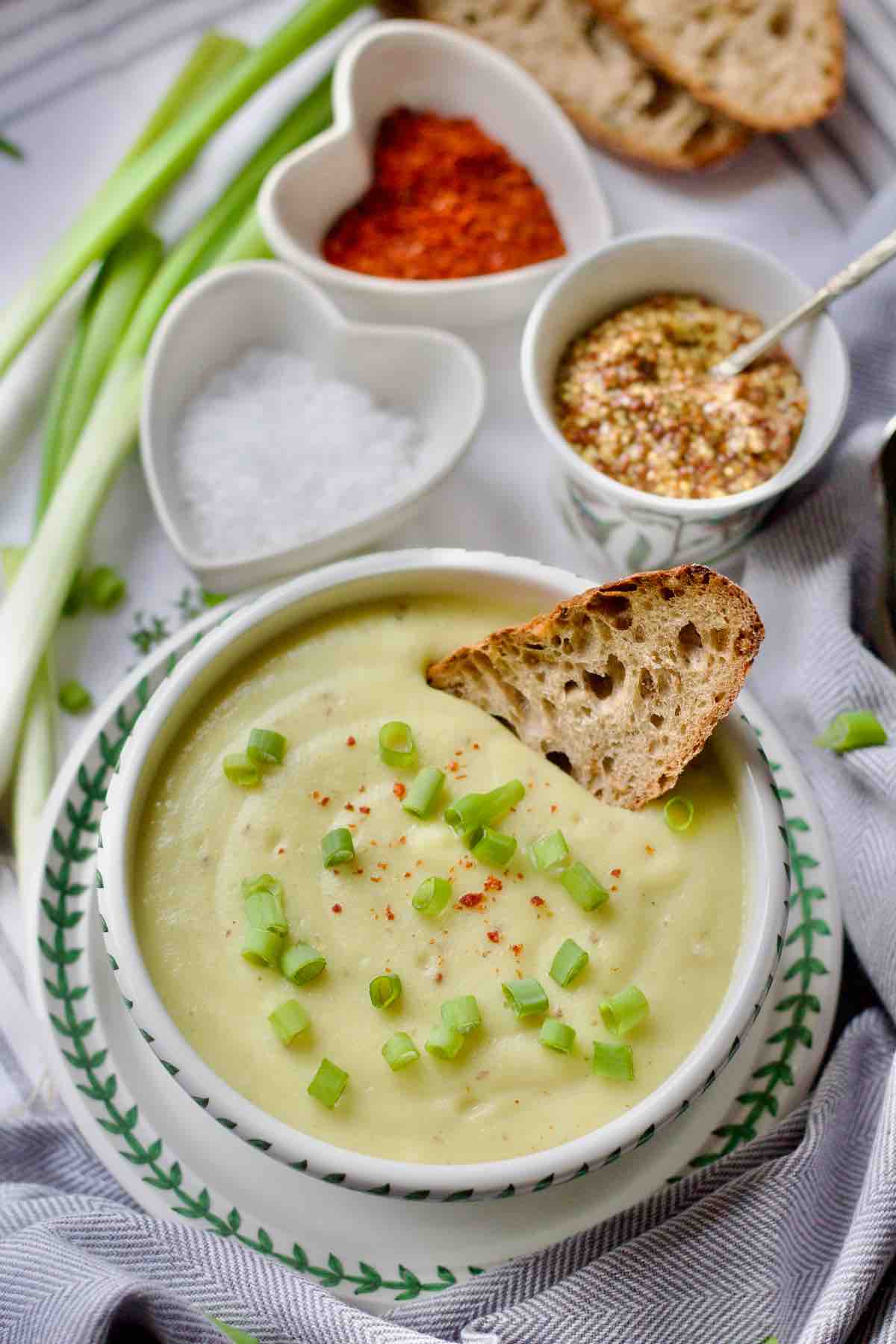 Served portion of cauliflower leek and potato soup in a bowl with garnish and piece of bread in a soup.