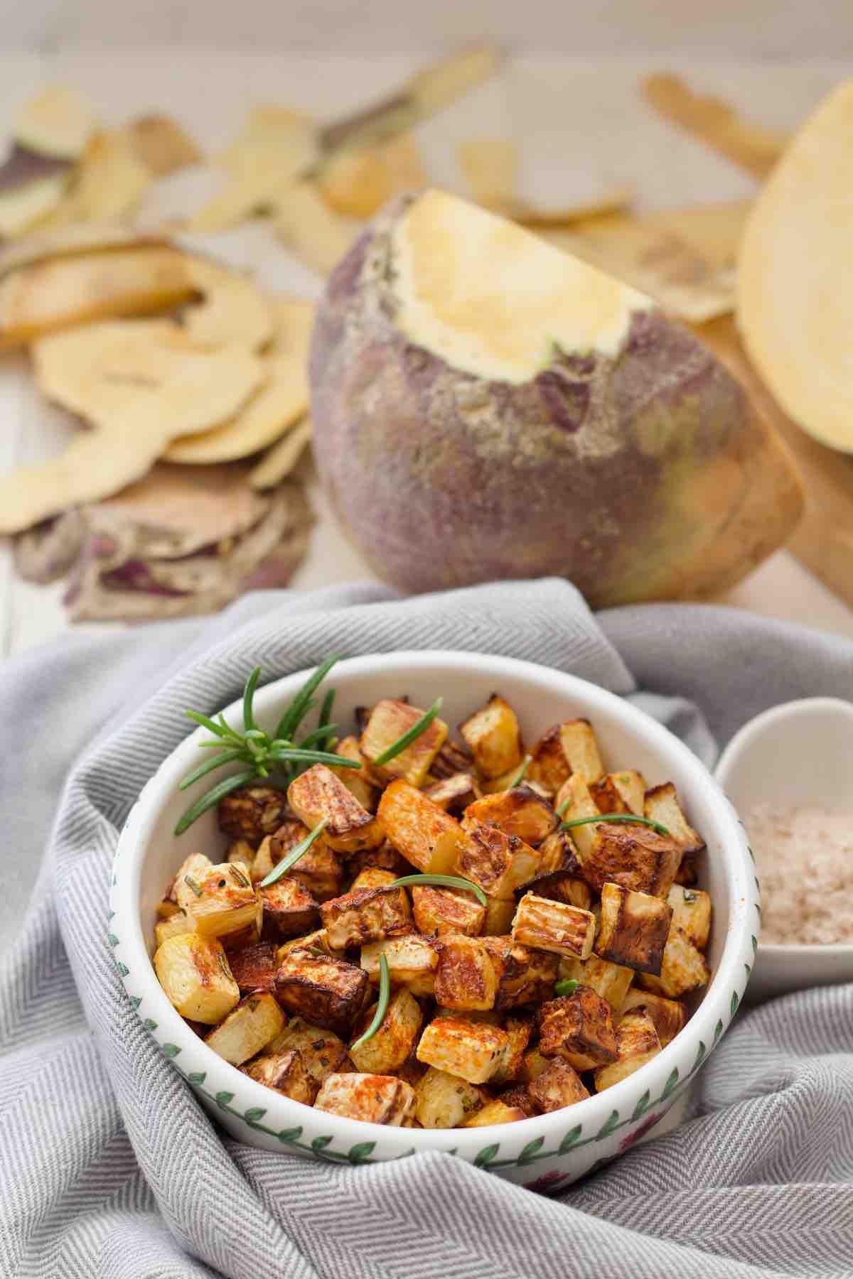 Roasted swede in a dish with raw swede and peelings behind it.