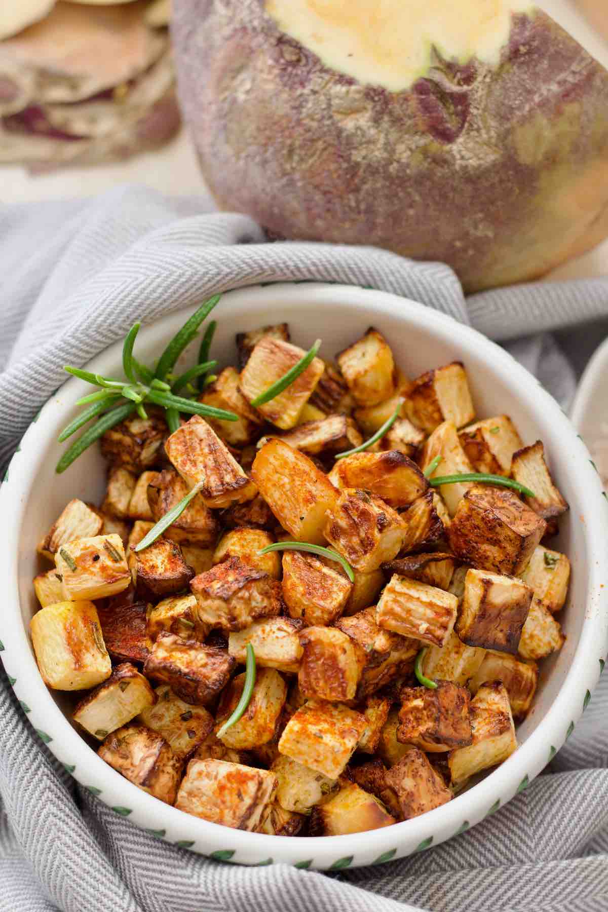 Roasted swede in a serving dish with some rosemary.