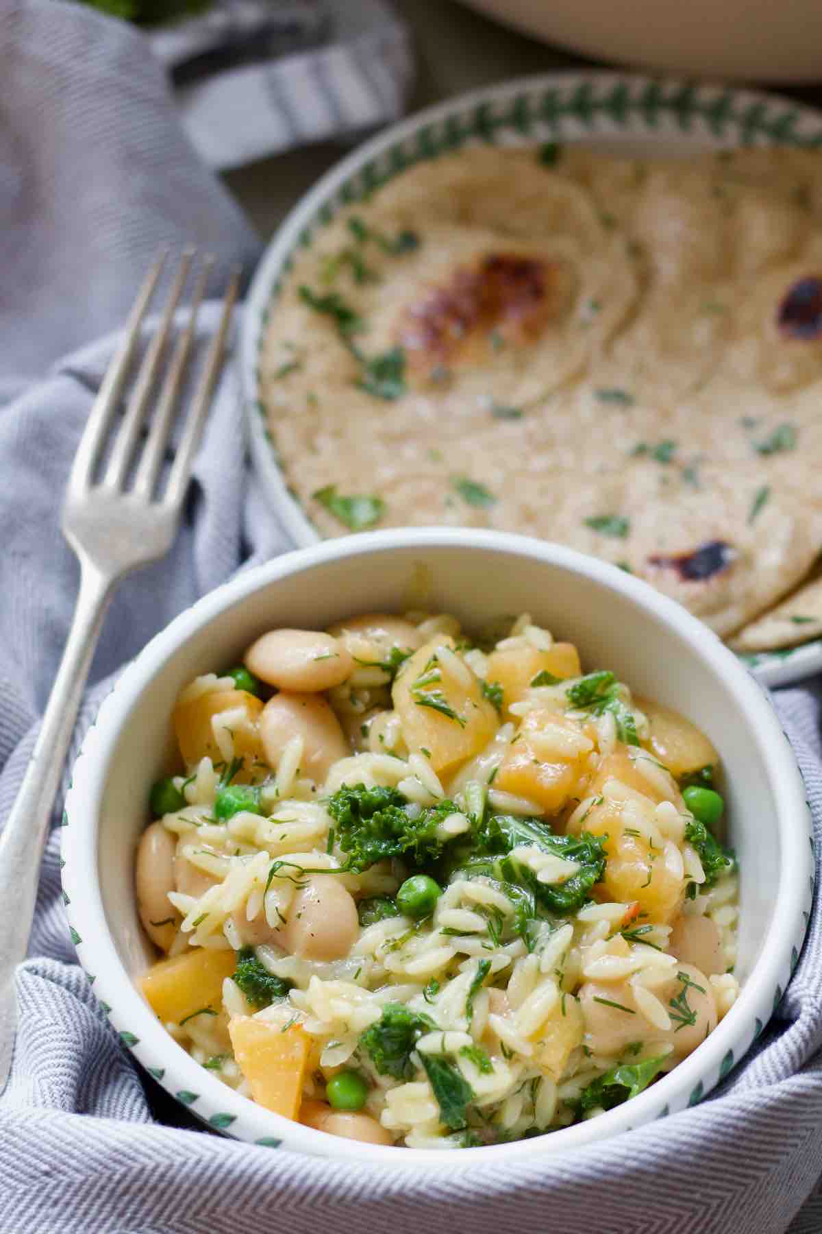 Bowl with portion of creamy braised swede orzo, garlic flatbread behind it.