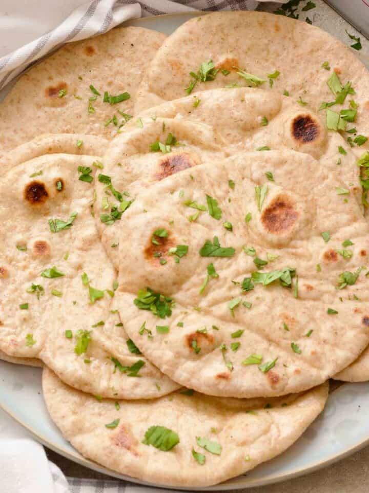 Close up of garlic flatbreads arranged on a plate, sprinkled with fresh parsley.