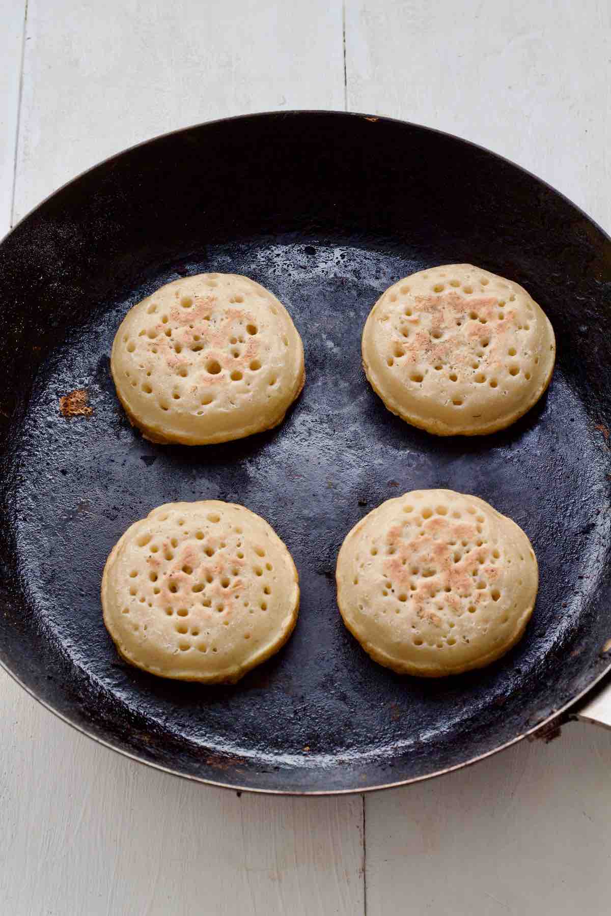 Four cooked crumpets in a pan.