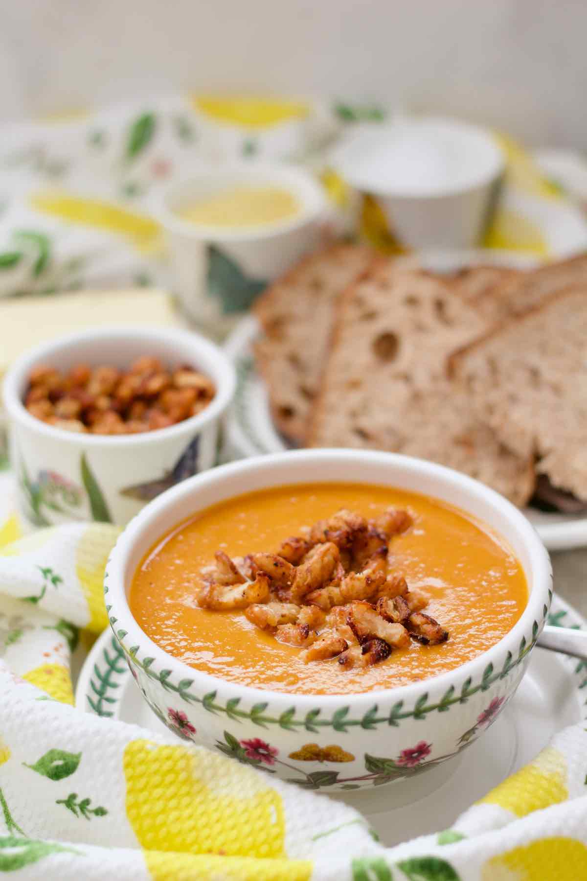 Soup in a bowl with sliced bread and crispy beans in a background.