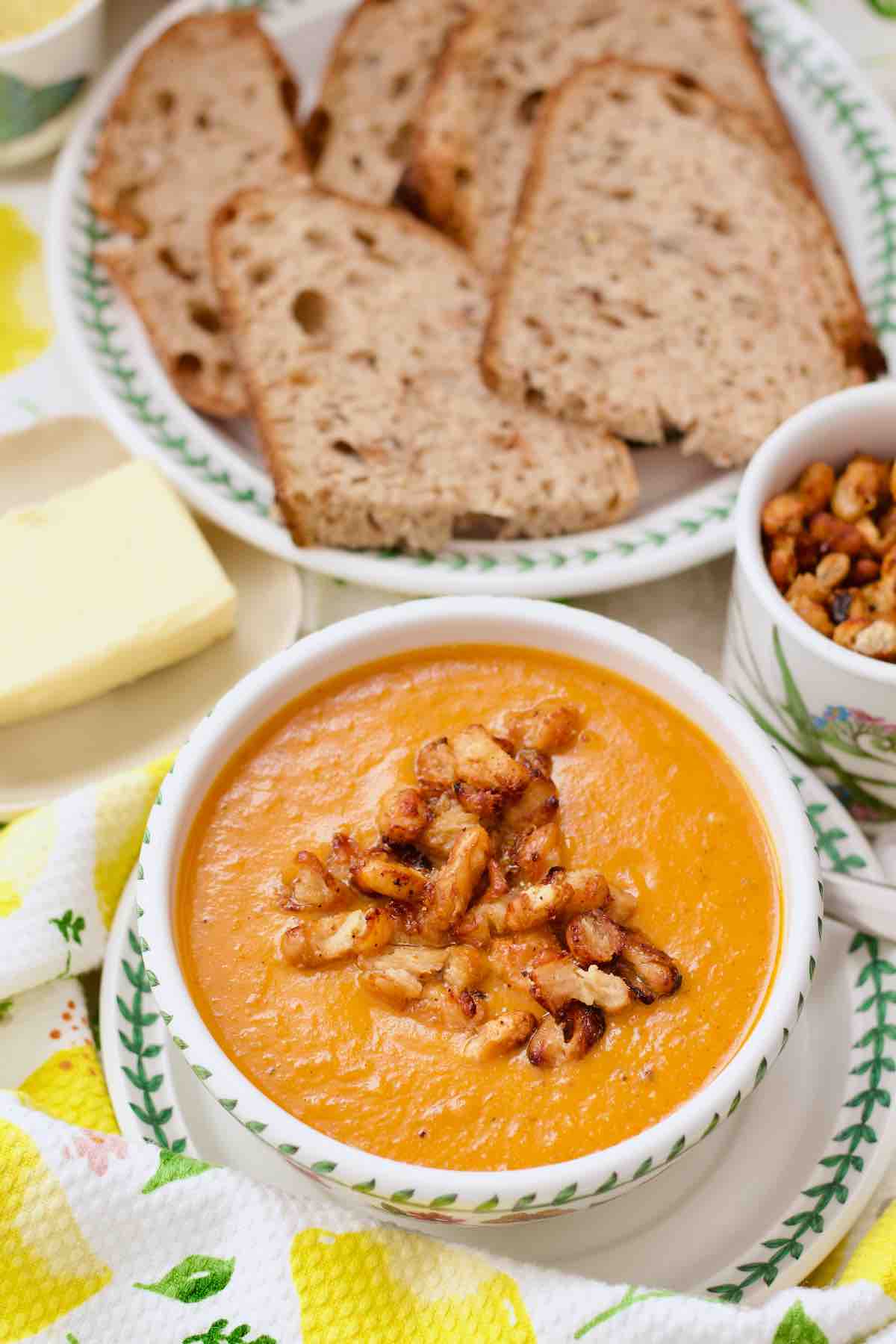 Roasted tomato and sweet potato soup served in a bowl with bread and crispy beans.