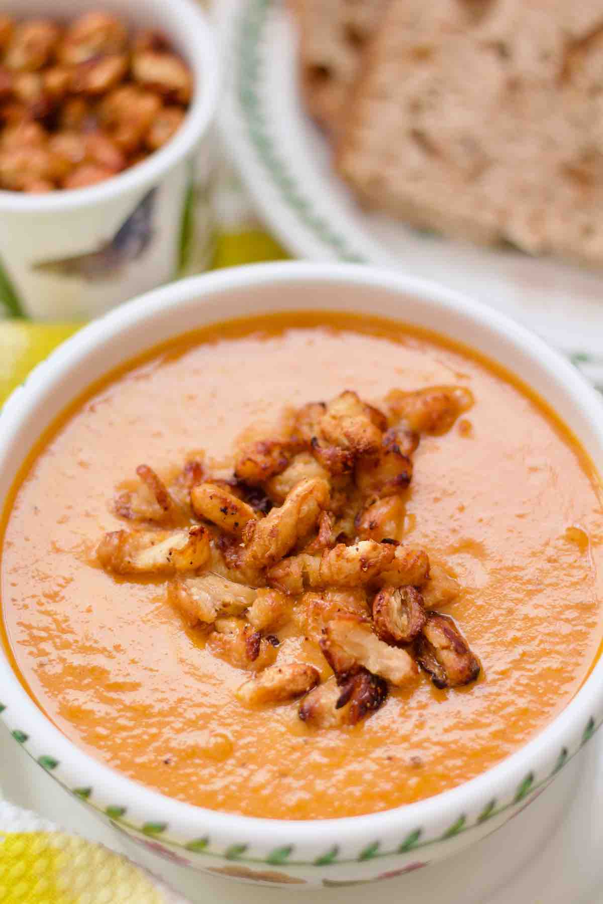Close up of tomato and sweet potato soup in a serving bowl with crispy beans on top.