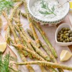 Square photo of asparagus tempura served with sauce and lemon wedges.