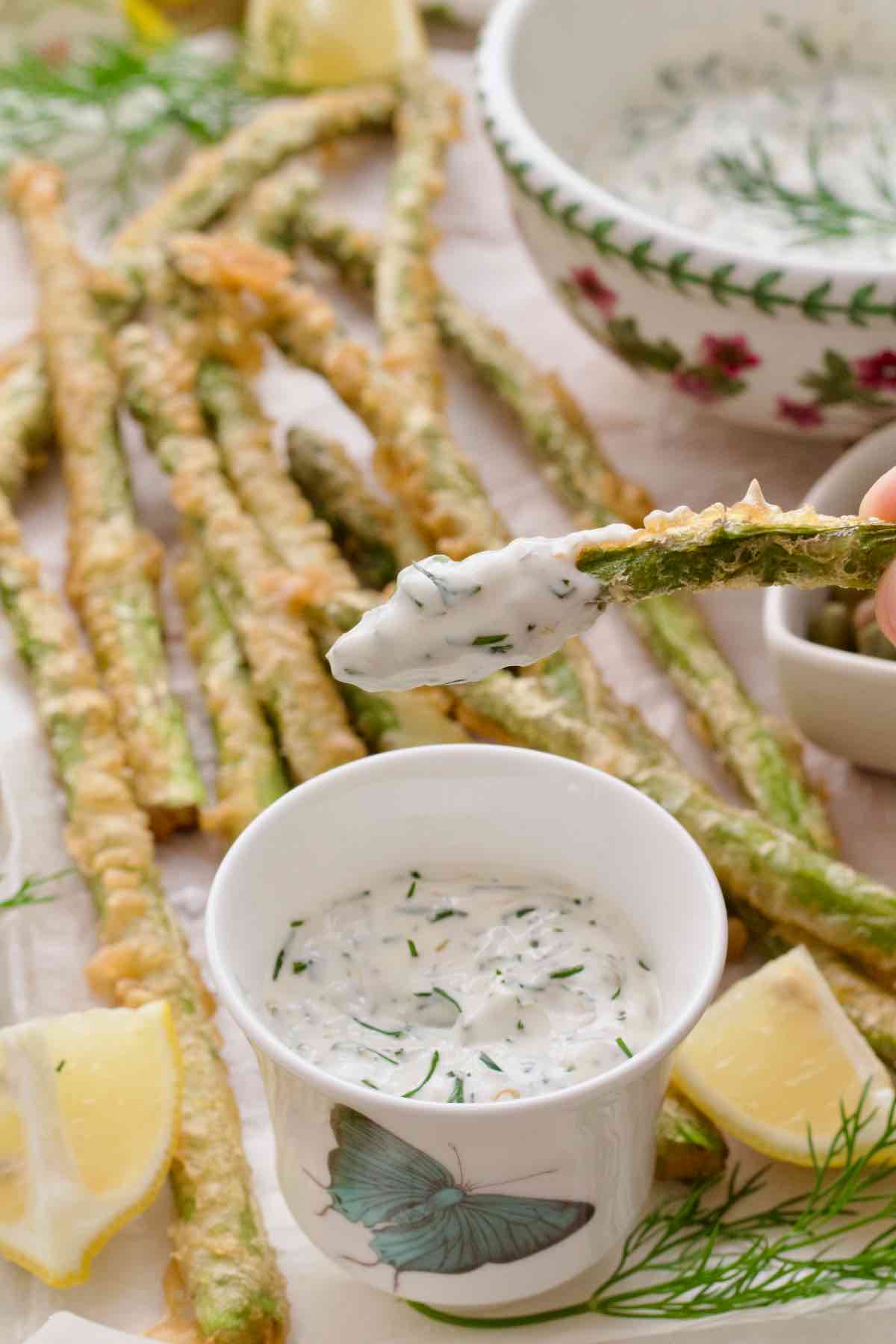 Piece of asparagus tempura dipped in tartar sauce.