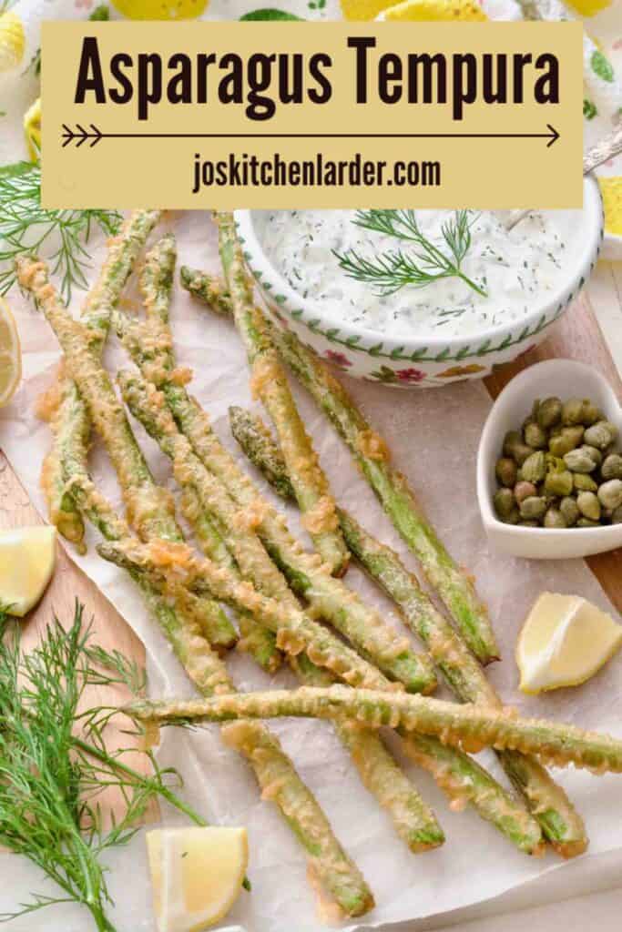 Asparagus tempura presented on a board covered with paper with tartar sauce and lemon wedges.