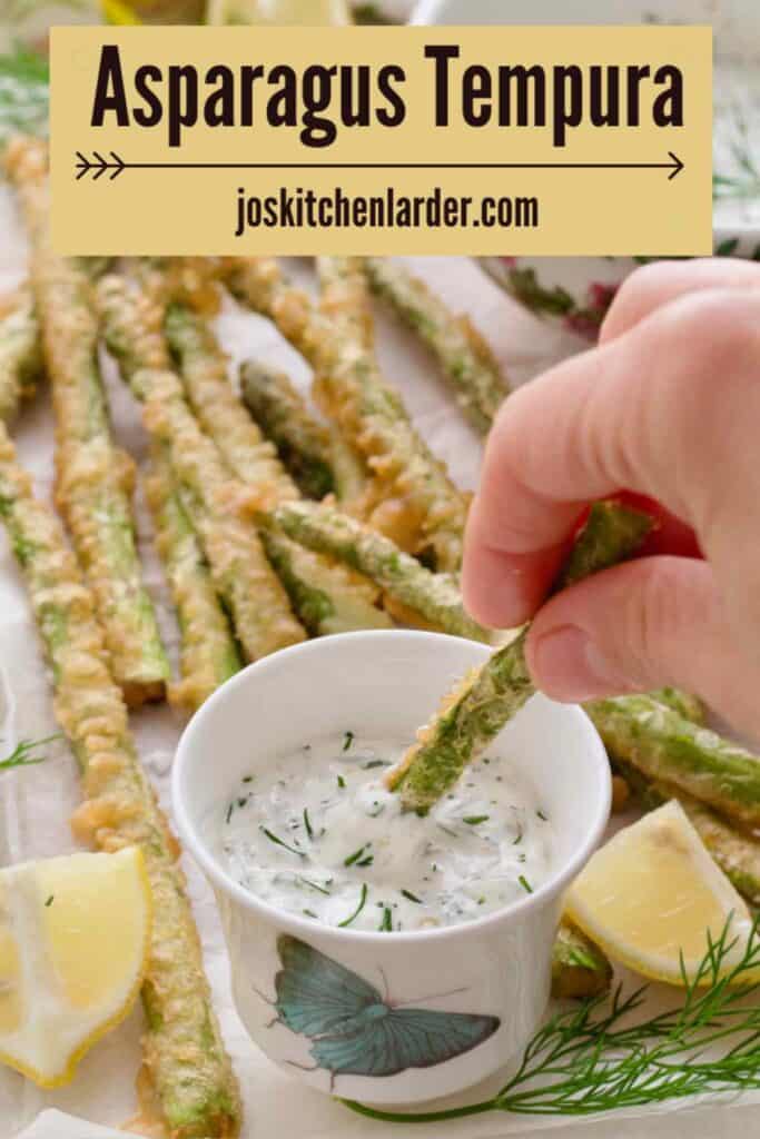 Hand dipping asparagus tempura in a small bowl with tartar sauce.