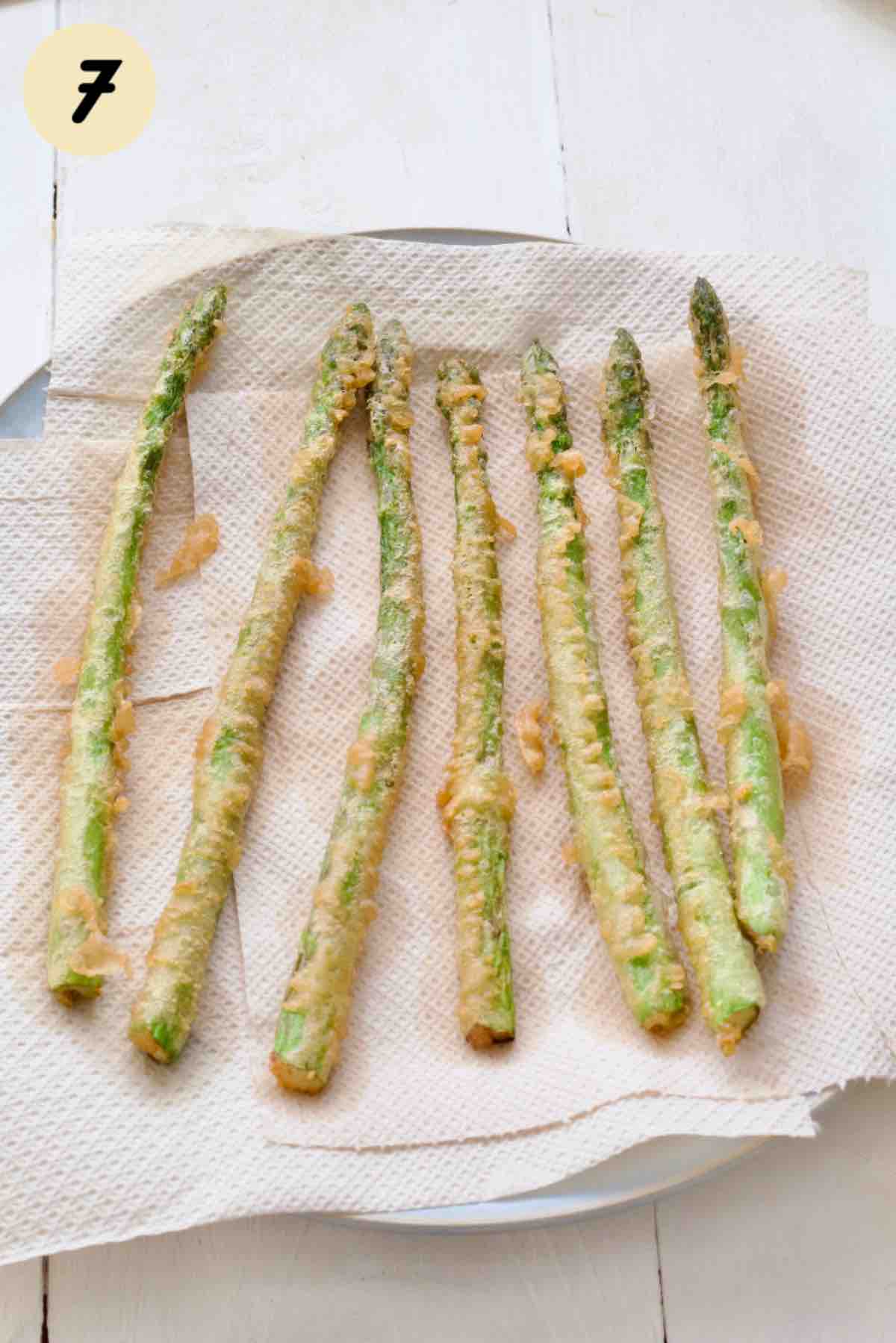 Fried asparagus spears draining on a plate covered with paper towels.
