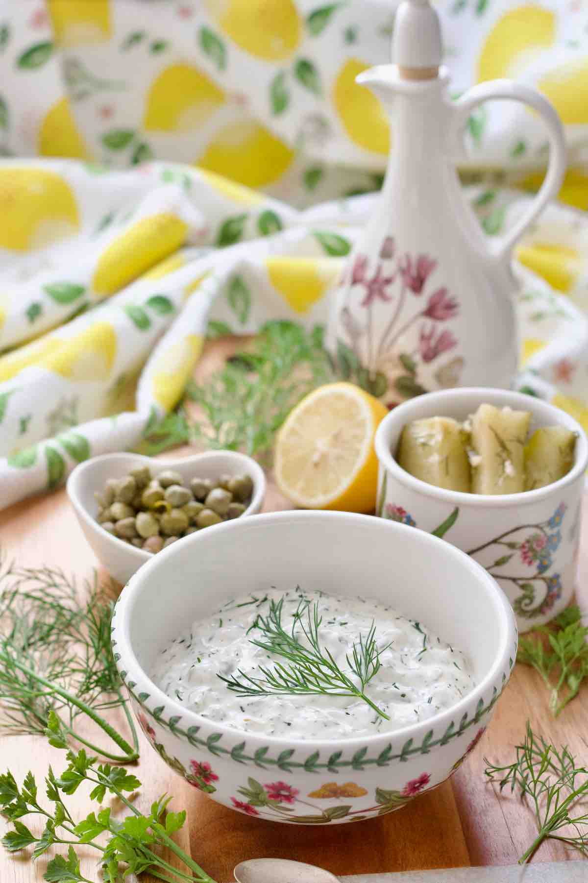 Tartare sauce in a bowl with gherkins, capers and lemon behind.
