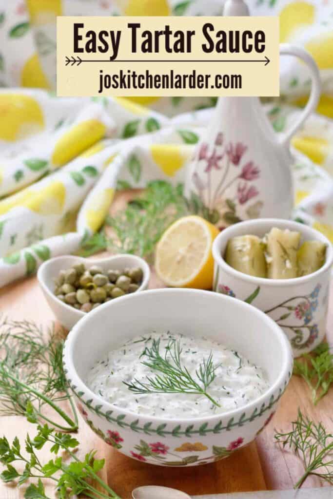 Tartare sauce in a bowl with gherkins, capers and lemon behind.