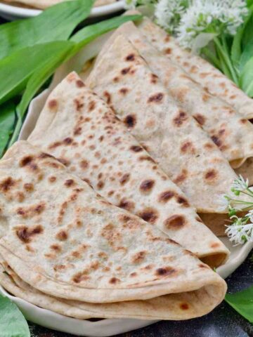 Close up of folded parathas arranged on a platter with wild garlic.