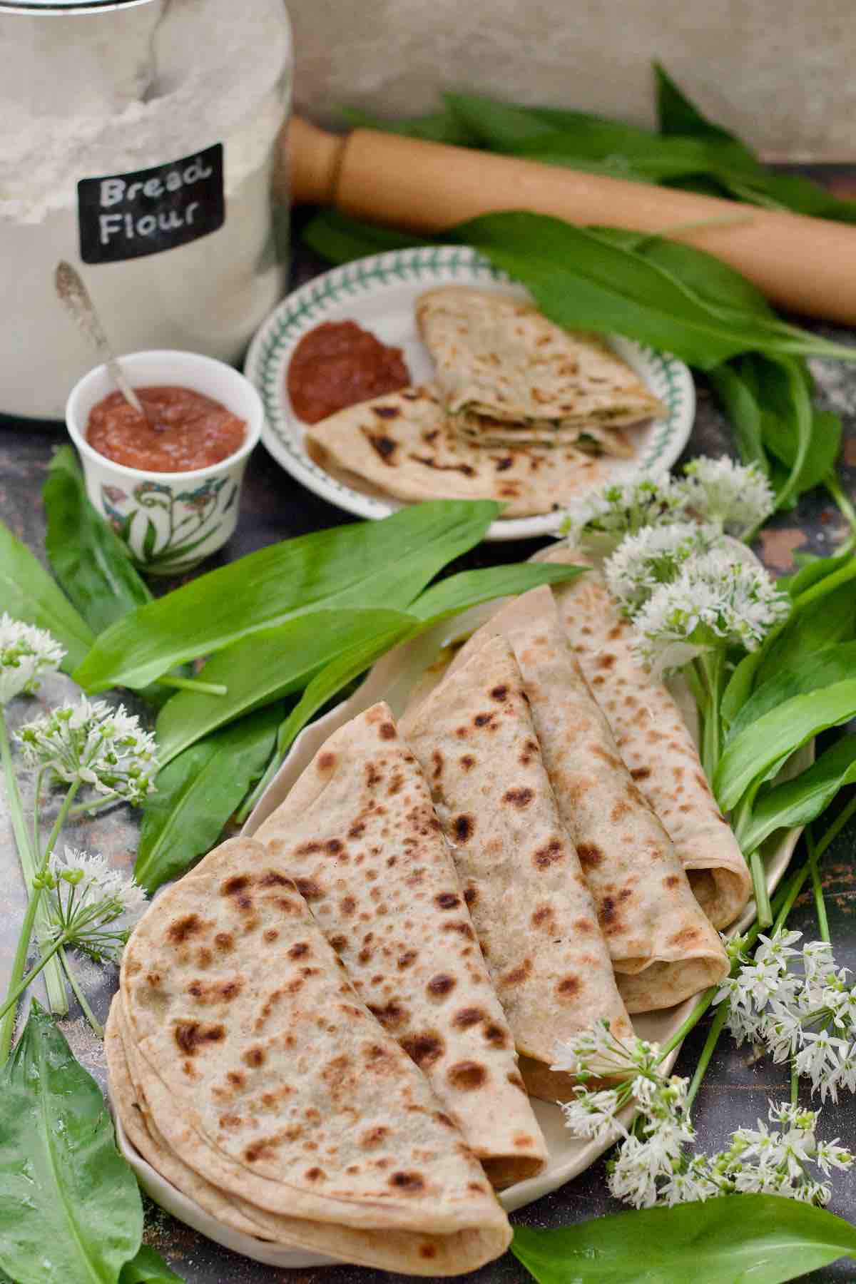 Platter with folded parathas, chutney and served paratha on a plate.