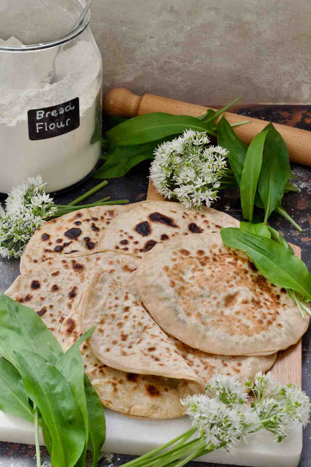 Wild garlic and potato parathas on a board with wild garlic around.