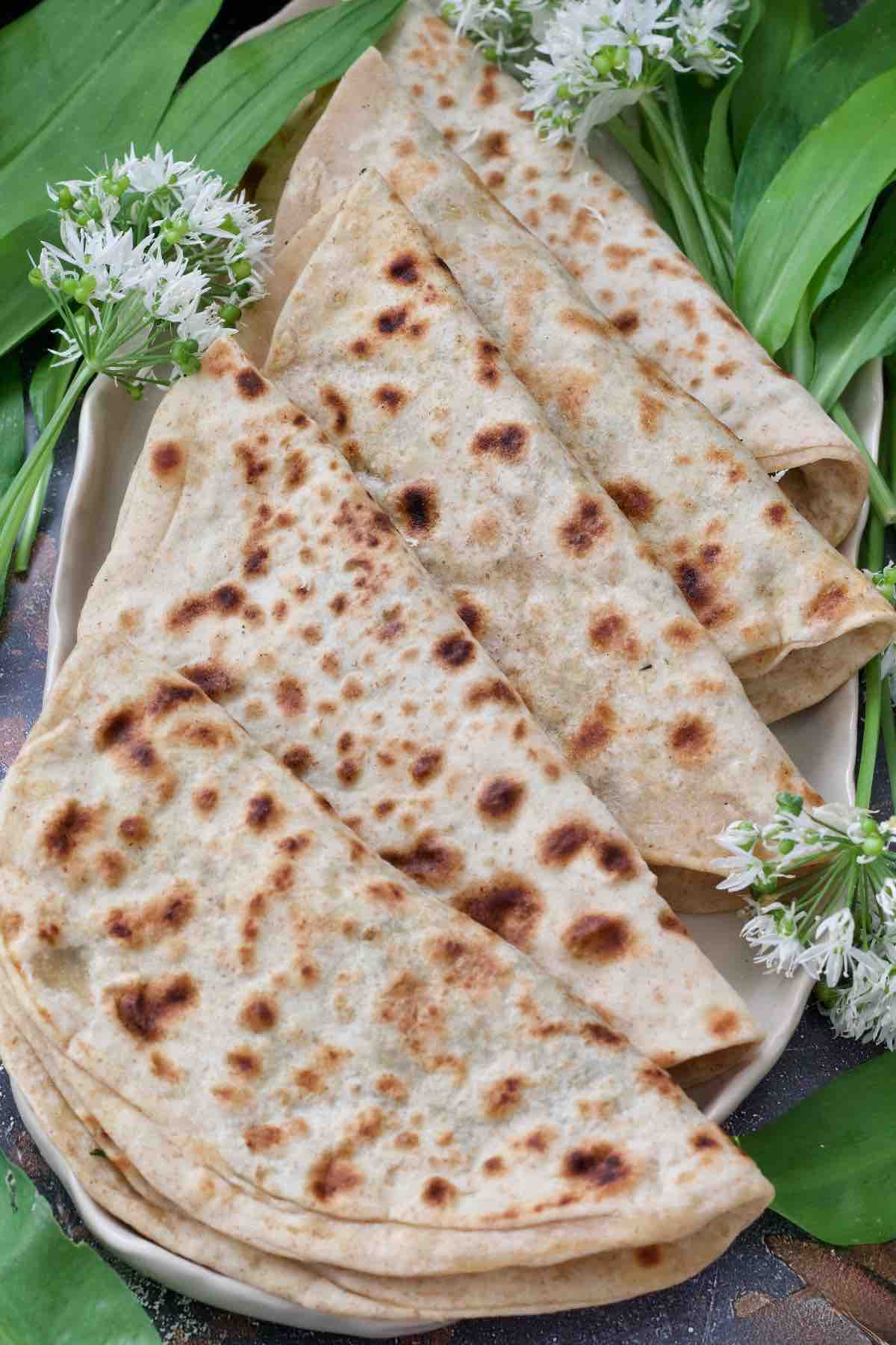 Five folded aloo parathas arranged on a platter with wild garlic.