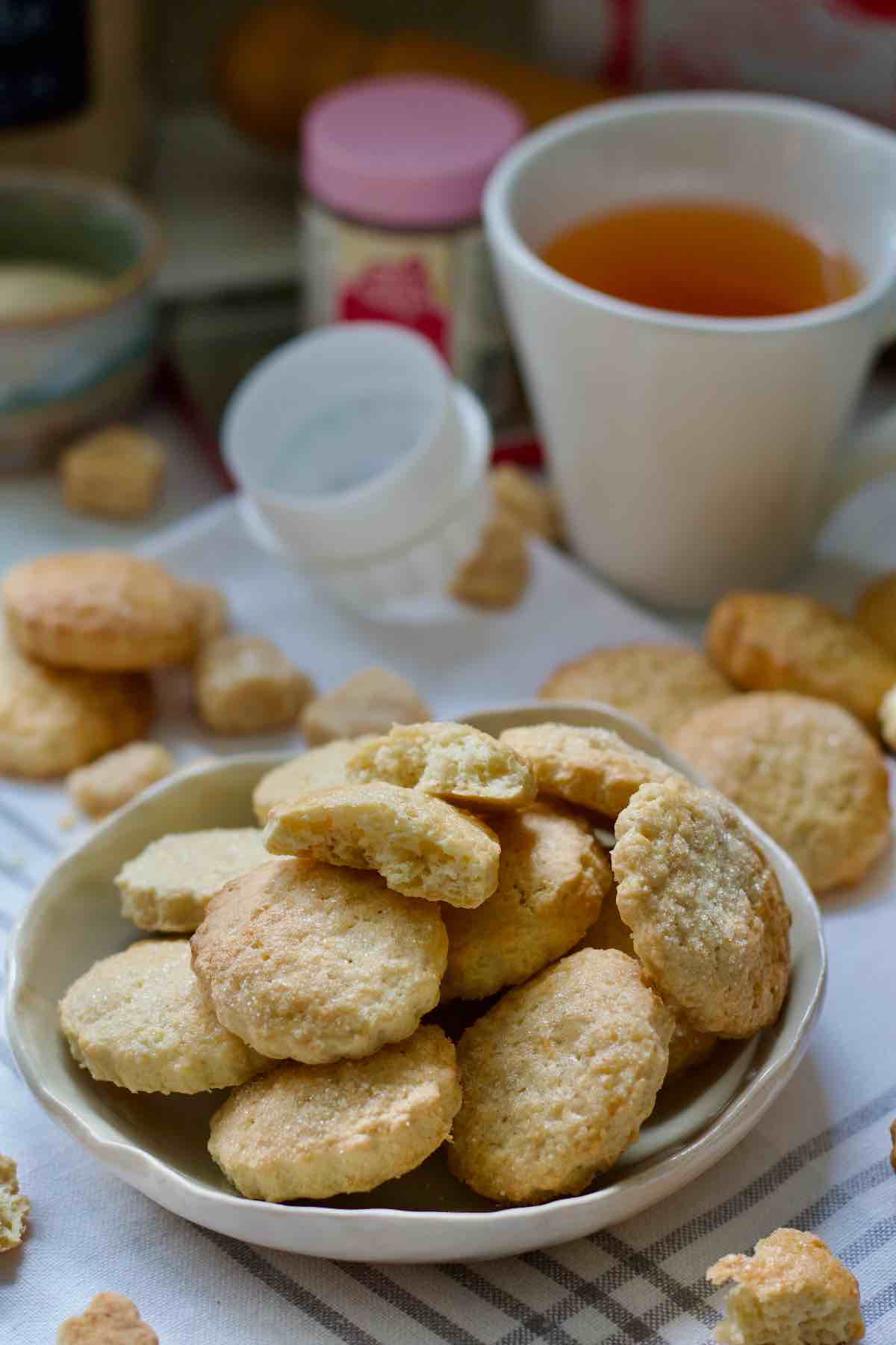 Plate of ammonia cookies, cookies scattered around and a cup of tea.