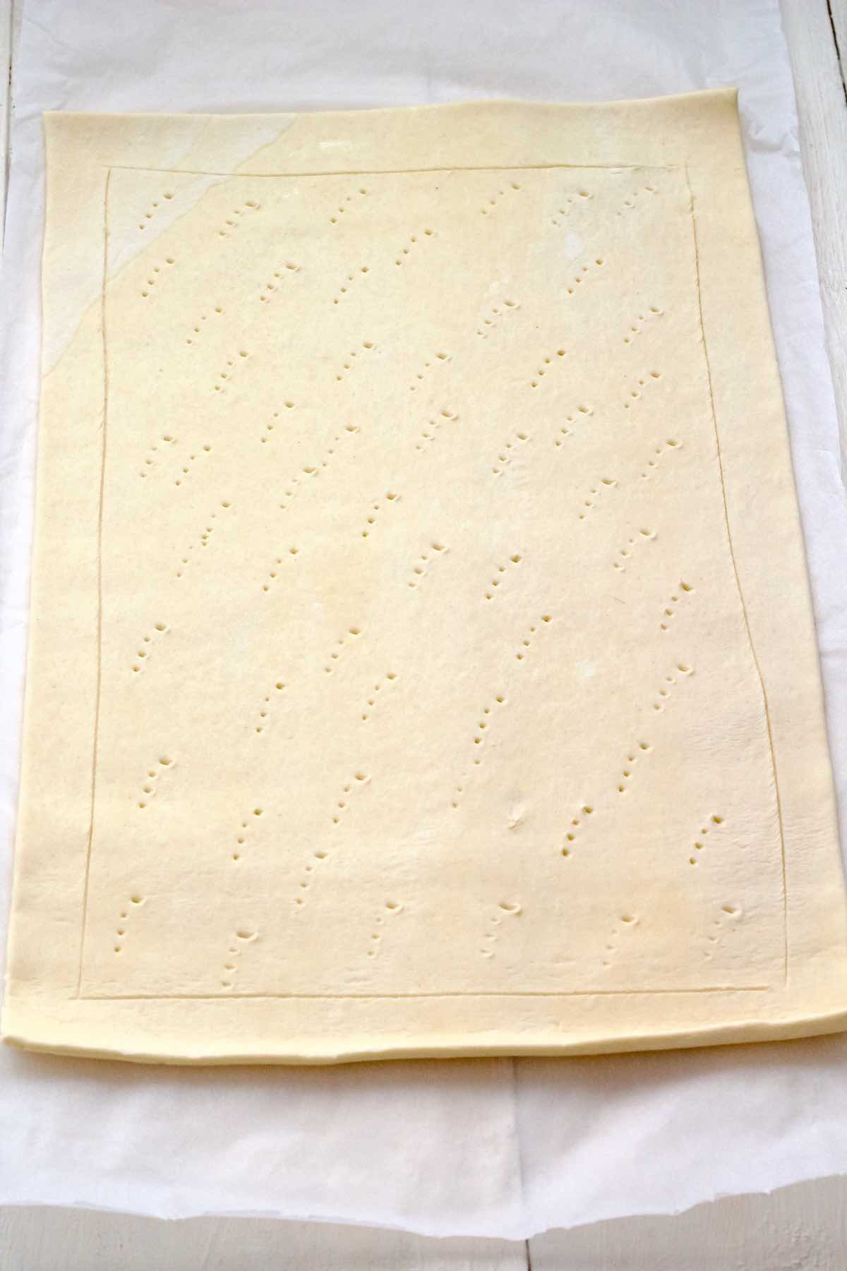 Puff pastry sheet with scored edge and middle pricked with a fork.
