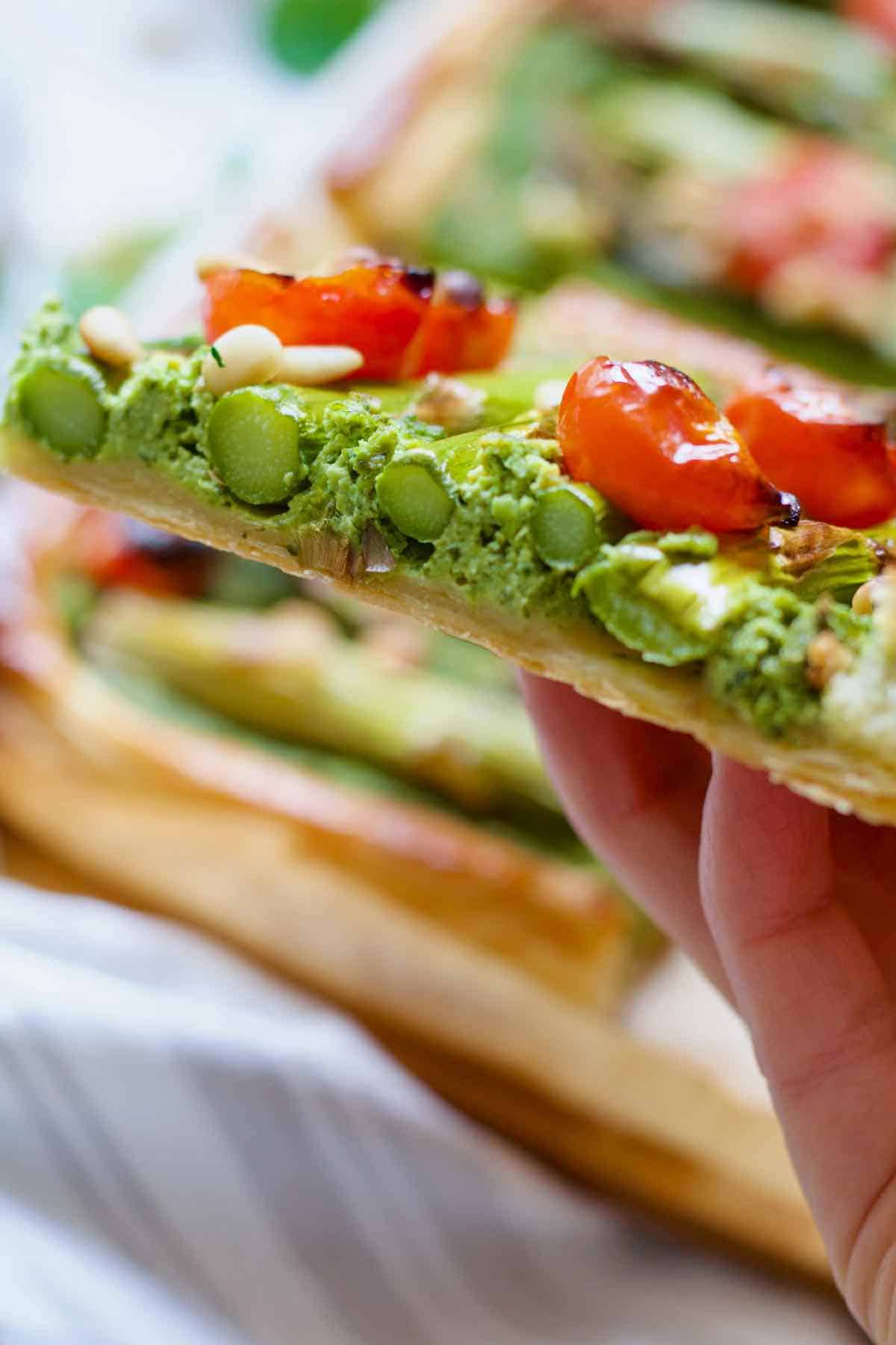 Hand holding cut piece of asparagus tart showing its cross section.