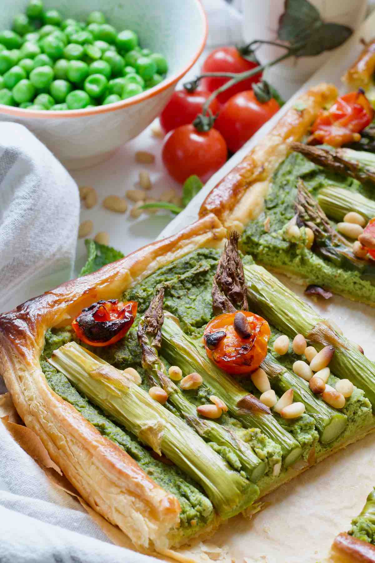 Asparagus tart square, peas in a bowl and cherry tomatoes.