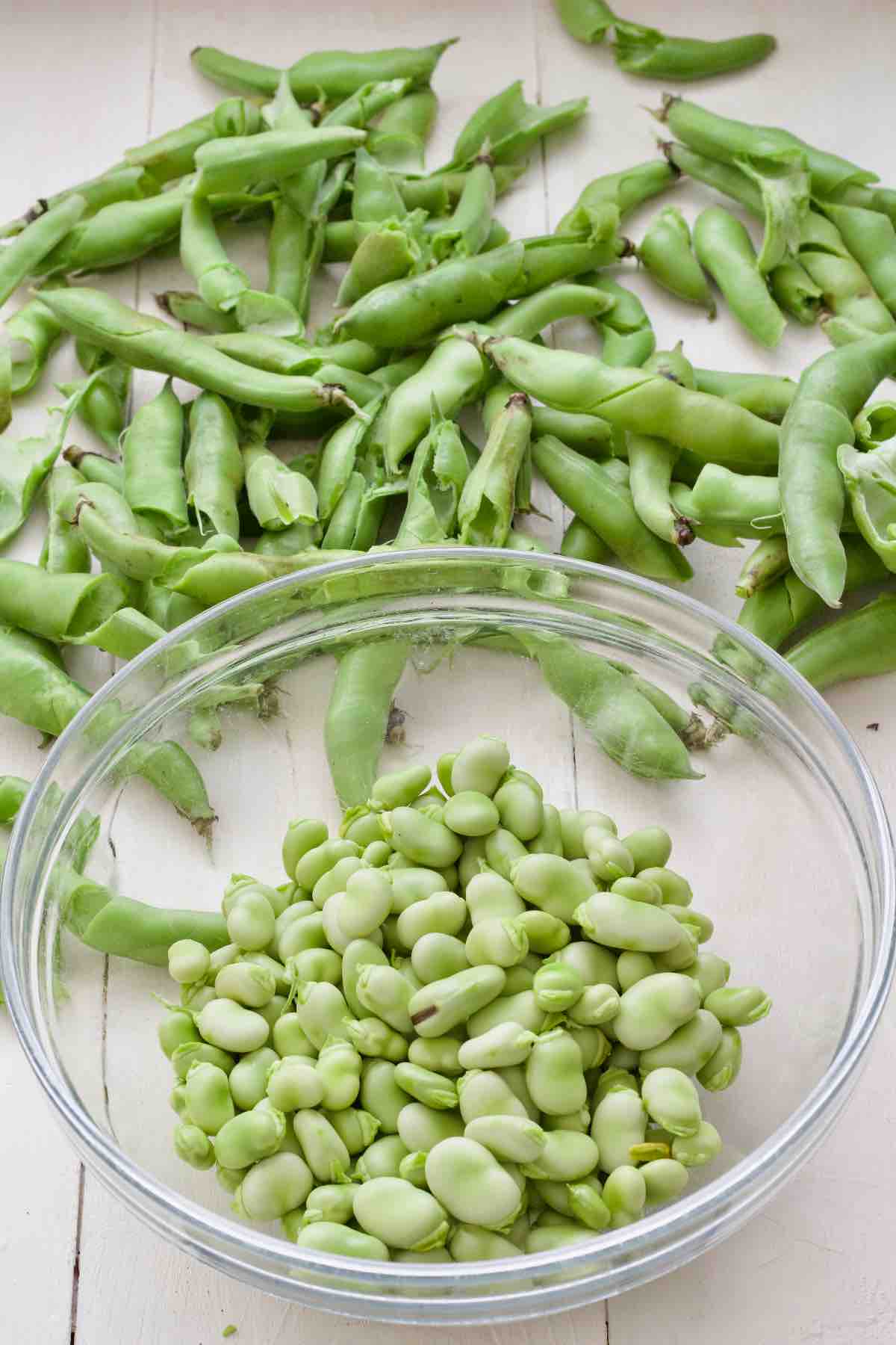 Podded broad beans in a bowl and pods scattered around.