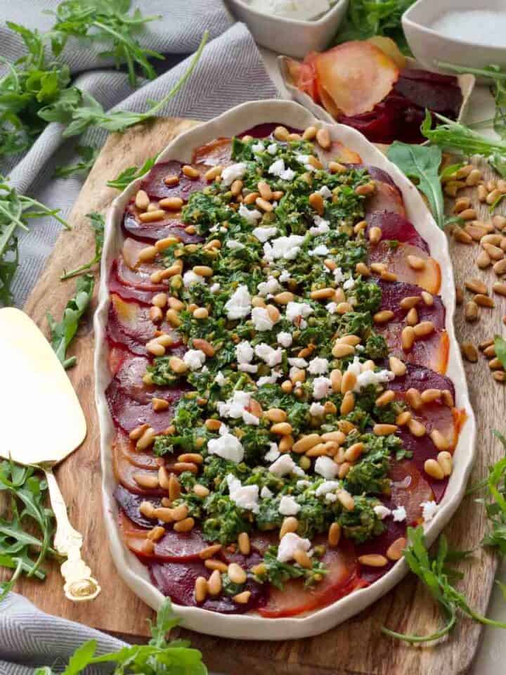 Square photo of beetroot carpaccio with rocket salsa on a platter with serving spoon ready to serve.